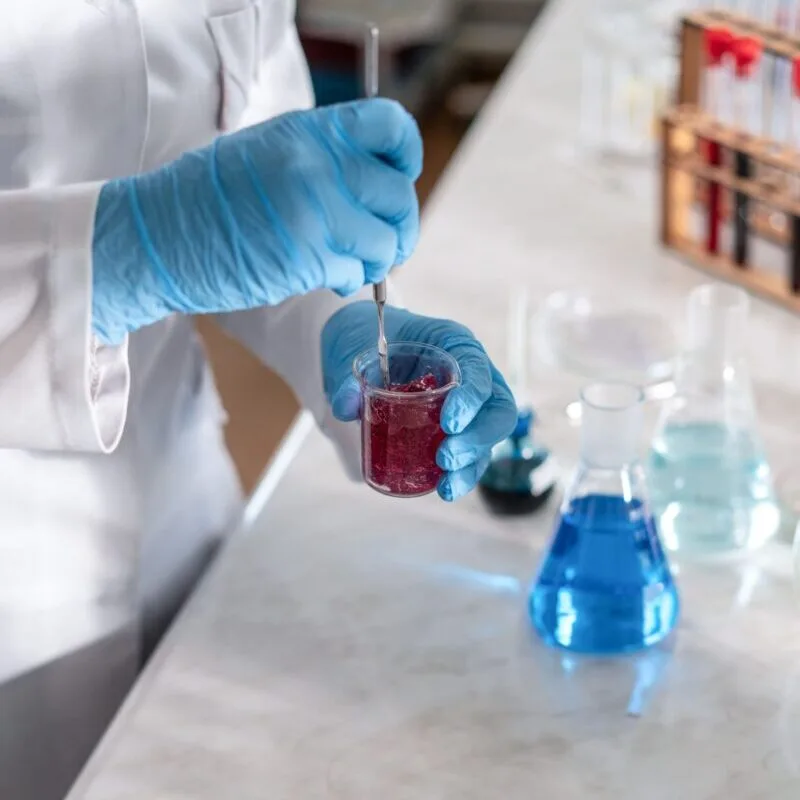 Scientist wearing gloves mixing chemicals in laboratory setting.