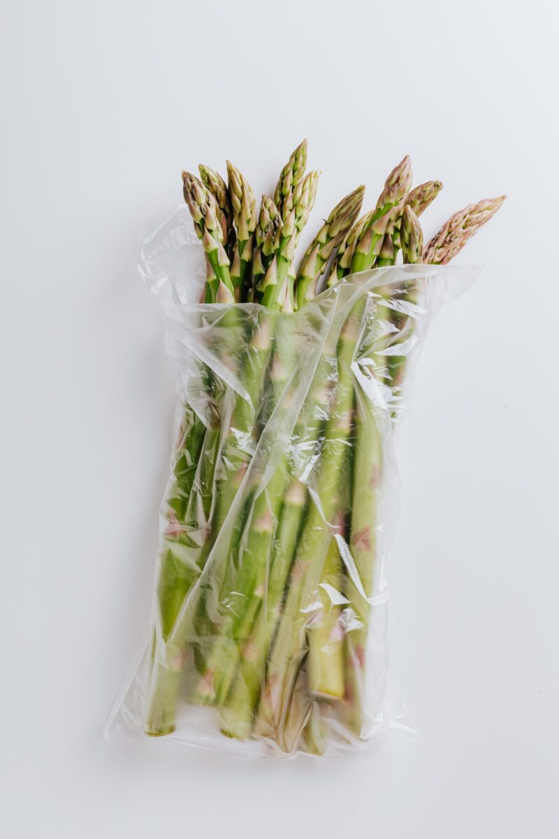 From above of bunch of fresh green asparagus stems placed in polyethylene bag isolated on white background